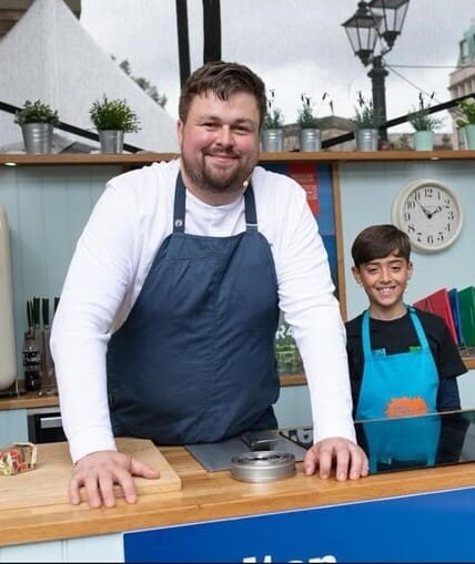Professional chef teaching young child how to cook at food festival